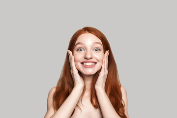 Keep smiling Portrait of cheerful pretty young redhead lady smiling at the camera while standing against grey background