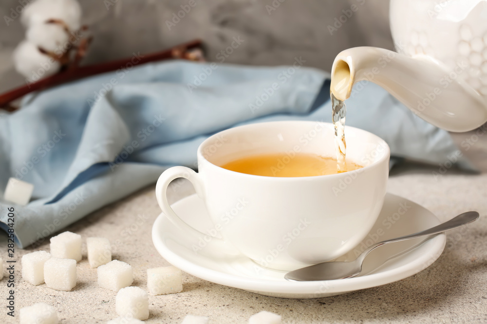 Pouring of hot tea in cup on table