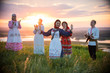 People in traditional russian clothes standing on the field on a background on the bright sunset - a woman dancing