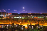 Fototapeta Las - Night city panorama with urban landscape and illuminated buildings under moon and night sky. Kiev