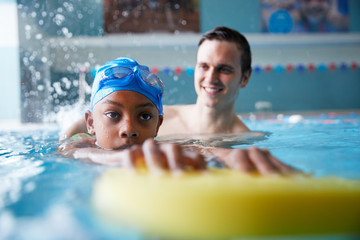 Wall Mural - Male Swimming Coach Giving Boy Holding Float One To One Lesson In Pool