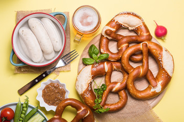 Pretzels, white bavarian sausages and vegetables on yellow background, german traditional food, oktoberfest