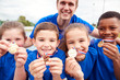 © Monkey Business - Portrait Of Children With Male Coach Showing Off Winners Medals On Sports Day
