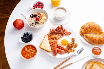 Wall Mural - Top view flatlay with varieties of fresh breakfast: fried eggs with bacon and sausages, oatmeal with berries, fried toasts with jam and butter. White background.