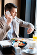 © LIGHTFIELD STUDIOS - businessman talking on smartphone and looking at watch in cafe