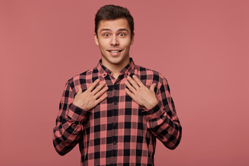 Wall Mural - Young handsome amazed guy wears in checkered shirt, looks at the camera with happy expression, point at himself, isolated over pink background.