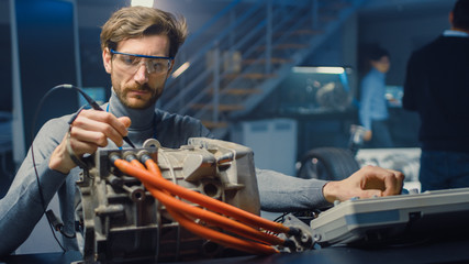 Fototapete - Professional Automotive Engineer in Glasses with a Computer and Inspection Tools is Testing an Used Electric Engine in a High Tech Laboratory with a Concept Car Chassis.