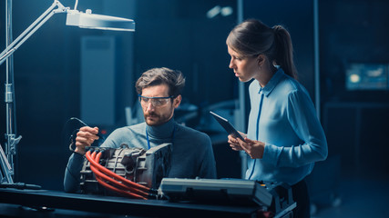 Fototapete - Male and Female Automotive Engineers with a Tablet Computer and Inspection Tools are Having a Conversation While Testing an Electric Engine in a High Tech Laboratory with a Concept Car Chassis.