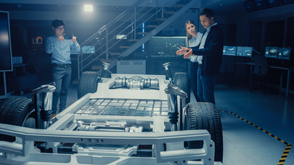 Poster - Automotive Design Engineers Talking while Working on Electric Car Chassis Prototype. In Innovation Laboratory Facility Concept Vehicle Frame Includes Wheels, Suspension, Engine and Battery.
