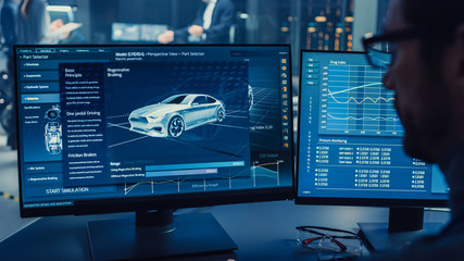 Wall Mural - Professional Engineer Works on a Computer with a 3D CAD Software and Tests the Electric Car Chassis Prototype with Wheels, Batteries and Engine Standing in a High Tech Development Laboratory.