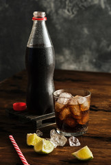 Glass with ice and fizzy beverage and bottle with carbonated drink