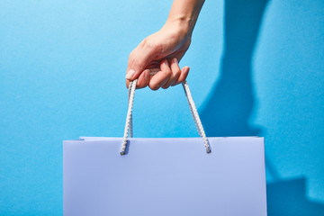 cropped view of woman holding purple shopping bag on blue