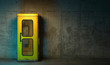 Single old yellow phone booth in retro style standing on the floor in front of the concrete wall at night time. Gloomy poorly lit interior in loft style with copy space. 3D rendering