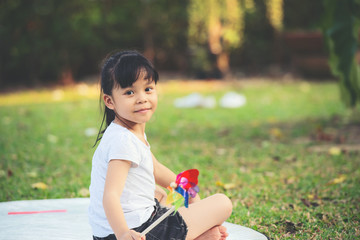 Wall Mural - Smiling a little asian girl sitting on green grass outdoors