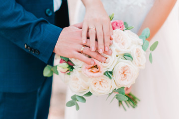 hands of bride and groom with wedding rings on beautiful bouquet of roses.