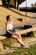 © Westend61 - Smiling young woman with headphones and smartphone sitting on bench enjoying sunlight