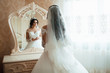 Beautiful young bride looking into the mirror having put on wedding dress. Beautiful young girl bride with fashion wedding hairstyle. A pretty and young bride is reflected in the mirror.