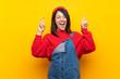 © luismolinero - Young Mexican woman with overalls over yellow wall with fingers crossing