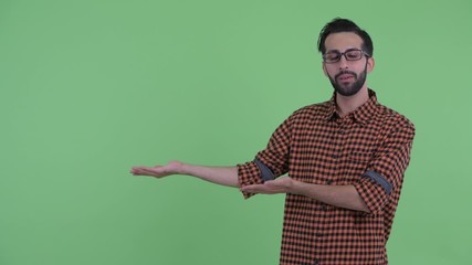 Wall Mural - Happy young bearded Persian hipster man talking while showing something