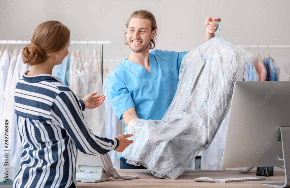 Male worker giving clothes to client in modern dry-cleaner's