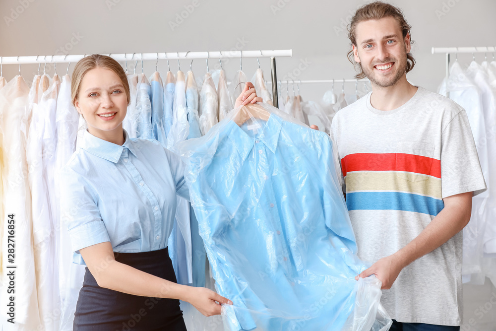 Worker giving clothes to client in modern dry-cleaner's