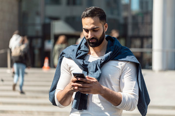 Wall Mural - Businessman looking at his mobile phone while walking on street to office