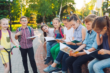 Happy Schoolmates Portrait. Schoolmates seating with books in a wooden bench in a city park and studying on sunny day.