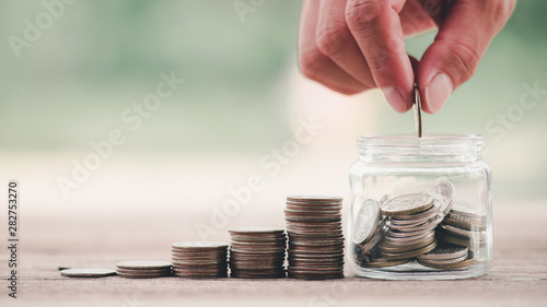 Cuadros en Lienzo Close up of stacking coins with hand putting Money in the jar on wooden table