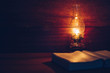 Close up of oil lamp with blurred holy bible on wood table in dark room, bible study or vintage book concept