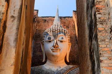 View of an ancient Buddha statue through the gate to Temple Wat Si Chum in Sukhothai Historical Park, Thailand ~ A giant sitting Buddha image with the posture of Subduing Mara inside a buddhist shrine