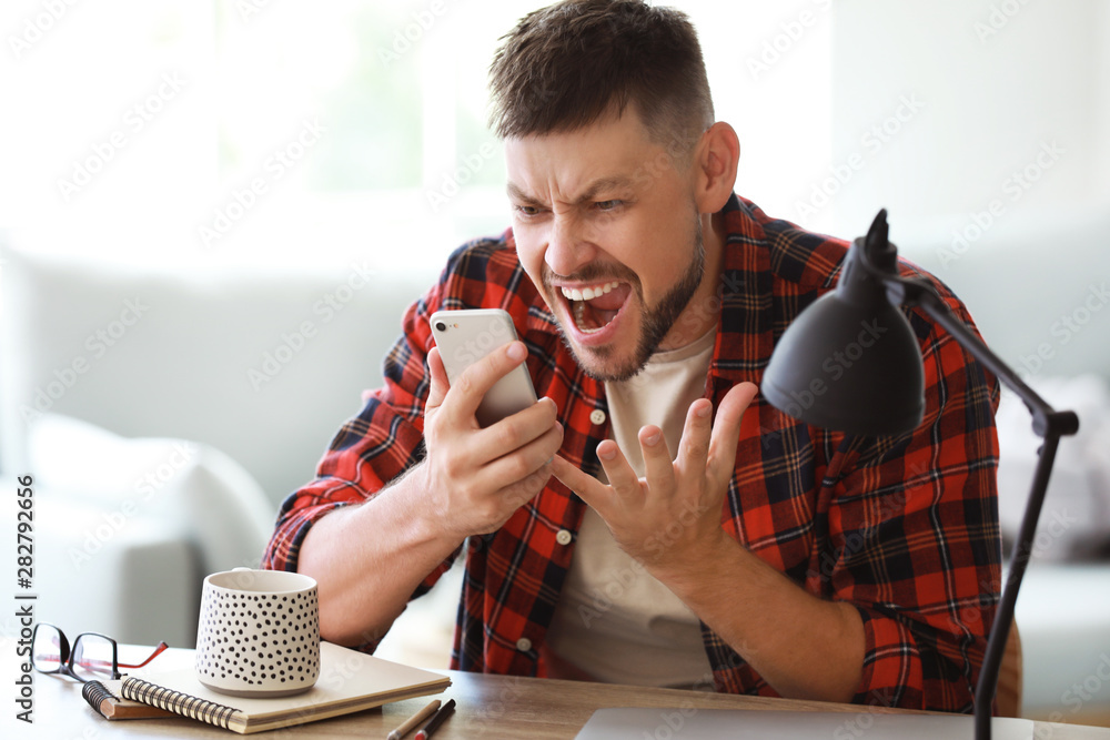 Stressed man talking by mobile phone at table in office