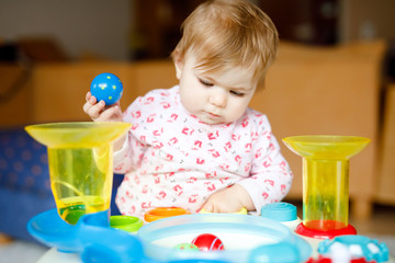 Adorable cute beautiful little baby girl playing with educational toys at home or nursery. Happy healthy child having fun and sorting colorful different plastic balls. Kid learning different skills