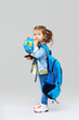 © oes - Smart child. Cute preschool girl with a blue backpack on her back, holding a globe in her hands. Preparing to study geography. The first time in first class. Space for text on neutral grey background