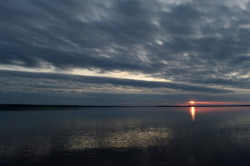 Wall Mural - Sunbeam on lake water at sunset from a solar flare in the dark clouds of the sky