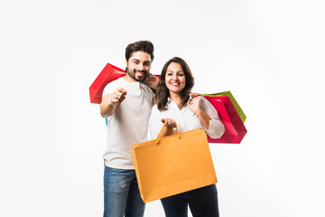 Indian young couple shopping bags and blank debit/credit or electronic card for payment, standing isolated over white background. selective focus