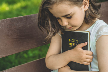 Wall Mural - Reading the Holy Bible in outdoors. Christian girl holds bible in her hands sitting on a bench. Concept for faith, spirituality and religion. Peace, hope