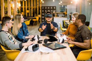 Group of young people employee workers having fun with vr virtual reality goggles in startup studio. Young Chinese man wearing VR glasses.