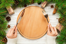 Top View Girl Holds Fork And Knife In Hand And Is Ready To Eat. Empty Wood Round Plate On Wooden Christmas Background. Holiday Dinner Dish Concept With New Year Decor