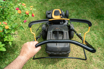 Wall Mural - Man hand holding a lawn mower machine to cutting green grass