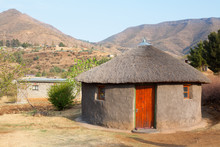 Traditional African Round Clay House With Thatched Roof In Village, Kingdom Of Lesotho, Southern Africa, Ethnic Basotho People National Old Home Close Up, Drakensberg Mountains Landscape Background