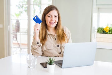 Poster - Beautiful young woman shopping online using laptop and credit card with a happy face standing and smiling with a confident smile showing teeth