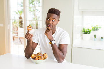 Canvas Print - African american man eating chocolate chips muffin serious face thinking about question, very confused idea