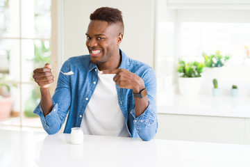 Poster - African american man eating healthy natural yogurt with a spoon very happy pointing with hand and finger