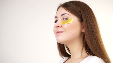 Sticker - Young woman applying golden collagen patches under eyes, against white. Mask removing wrinkles and dark circles. Girl taking care of delicate skin around eye. Beauty treatment