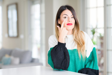 Sticker - Young beautiful woman wearing winter sweater at home Pointing to the eye watching you gesture, suspicious expression