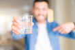 © Krakenimages.com - Young handsome man drinking a glass of water at home with surprise face pointing finger to himself