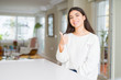 © Krakenimages.com - Young beautiful woman at home on white table doing happy thumbs up gesture with hand. Approving expression looking at the camera with showing success.