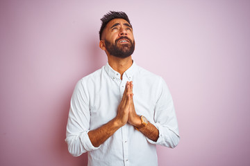 Wall Mural - Young indian businessman wearing elegant shirt standing over isolated pink background begging and praying with hands together with hope expression on face very emotional and worried. 