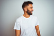 © Krakenimages.com - Young indian man wearing t-shirt standing over isolated white background looking away to side with smile on face, natural expression. Laughing confident.
