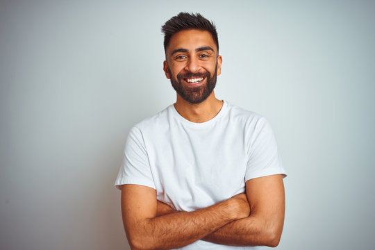 Young indian man wearing t-shirt standing over isolated white background happy face smiling with crossed arms looking at the camera. Positive person.
